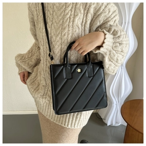 Detail of black pleated tote bag featuring gold floral hardware and slim crossbody strap