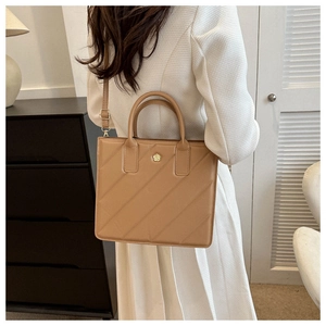 Brown quilted tote bag with golden flower logo and adjustable strap on a female model