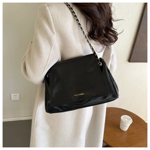 Détail du sac cabas en cuir noir avec bandoulière chaîne et lettrage doré sur manteau