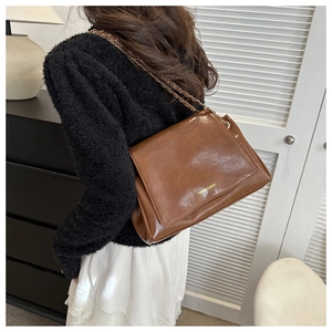 Détail du sac bandoulière en cuir caramel avec chaîne dorée et lettrage métallique