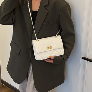 Sac à bandoulière matelassé blanc avec chaîne dorée porté par un mannequin en blazer vert