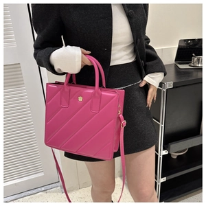 Detailed close-up of rose pink quilted tote bag with golden flower emblem on grey coat