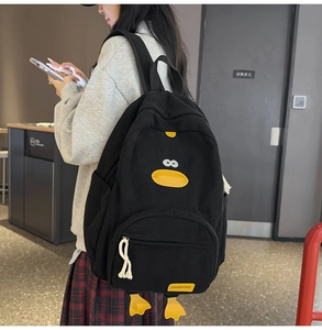 Detail of black corduroy backpack featuring cartoon duck design and fashion fabric label