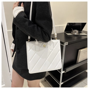 Close-up of white quilted tote bag with golden flower logo and adjustable shoulder strap