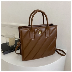 Close-up of dark brown quilted leather handbag with gold flower emblem on a white stand