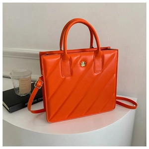 Detail of orange quilted handbag with floral gold emblem on white podium stand