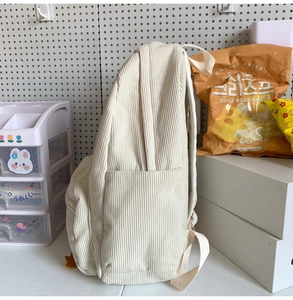Detail view of cream white corduroy backpack showing soft ribbed texture and side pocket