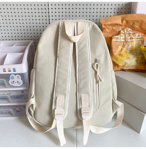 Back view of beige corduroy school backpack with adjustable straps on student desk