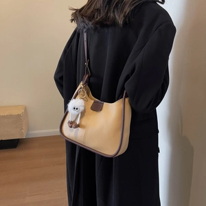 Minimalist khaki shoulder bag with brown trim and cute white plush charm on a model