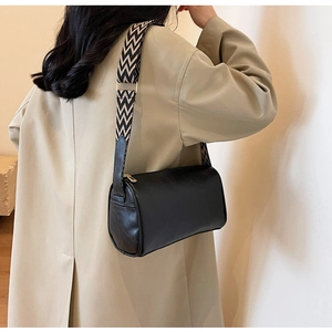 Détail du sac à bandoulière cylindrique noir avec sangle à motifs sur un trench-coat chic