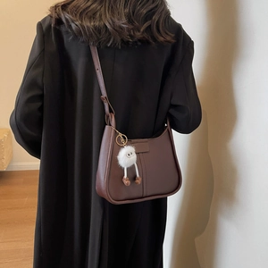 Deep brown leather saddle bag with plush doll charm worn by model in black wool coat