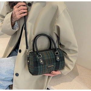 Détail du sac boston à carreaux vert et marron avec poignées en cuir et texture riche