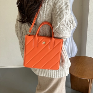 Quilted orange tote bag with floral metal accent and adjustable strap shown on model