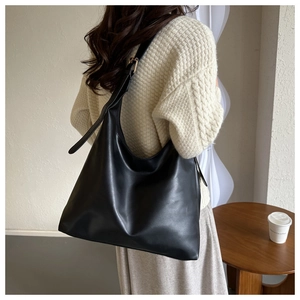 Detail of black matte leather tote bag with gold hardware shown on model's shoulder
