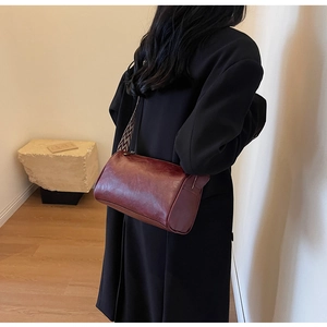 Détail du sac cylindre bordeaux avec une large bandoulière géométrique noire et blanche