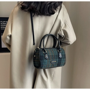 Détail d'un sac tonneau vintage à carreaux avec poignées en cuir et rivets en métal