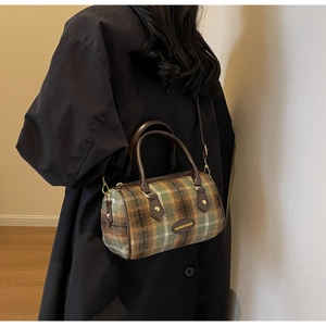 Détail du sac Boston en laine à carreaux verts porté sur un manteau noir avec bandoulière