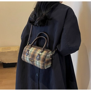 Détail du sac cylindrique rétro à carreaux montrant la texture tissée et la bandoulière en cuir