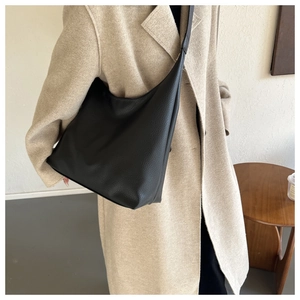 Detail of black lychee texture leather hobo bag worn with a beige cashmere coat