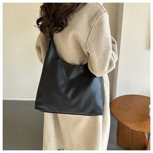 Close-up of a large black lychee leather tote bag worn by a model in a minimalist setting