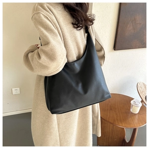 Detail of black pebbled leather tote bag with gold hardware worn by a model in a modern room