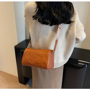 Gros plan d'un sac cylindrique marron rétro avec bandoulière à motifs et texture cuir