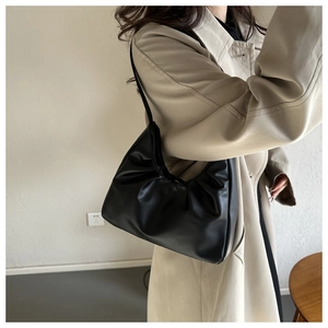Model wearing a black ruched shoulder bag with a stylish beige trench coat in a minimal setting