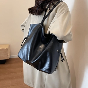 Minimalist black large capacity PU leather tote bag worn with a beige trench coat
