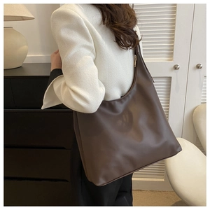 Detail of dark brown matte leather tote bag with gold zipper worn in a modern home setting