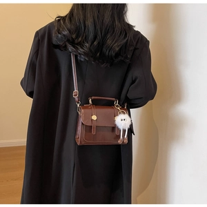 Rear view of brown leather square crossbody bag with white plush monster charm