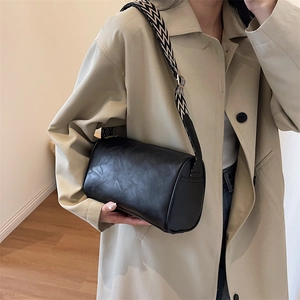 Sac polochon noir classique avec bandoulière à motifs porté par un mannequin en trench