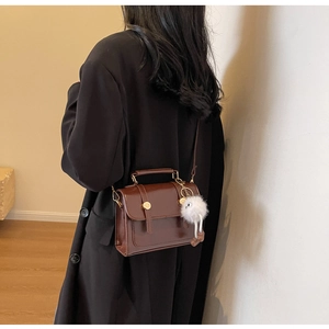 Detail view of brown vintage leather crossbody bag with a white plush pompom charm keychain