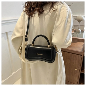 Détail d'un sac à main en cuir noir avec garniture dorée sur un manteau beige