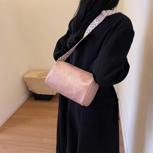 Sac à bandoulière cylindrique mauve avec large sangle à motifs porté sur un manteau noir