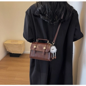 Close-up of a vintage brown oil wax leather crossbody bag with a white plush charm