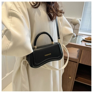 Détail d'un sac bandoulière en PU brillant noir avec logo doré sur un manteau blanc