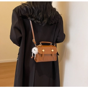 Brown matte leather crossbody bag with gold snap buttons and plush charm shown on model
