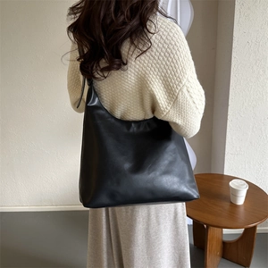 Minimalist black leather tote bag shown from a back perspective in a casual setting