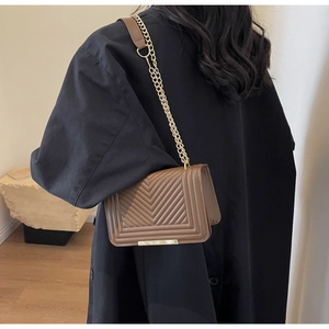 Detail of dark brown leather chain bag with V-quilted texture on black winter coat