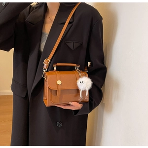 Brown vintage flap crossbody bag with white plush charm worn over a black blazer jacket