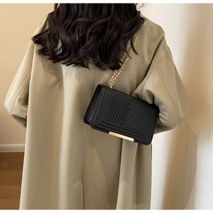 Rear view of model wearing a black quilted crossbody bag with gold chain strap