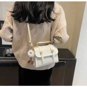 White leather crossbody bag with top handle and plush charm shown on a knit sweater