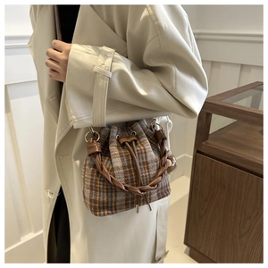 Close-up of woven leather handle and textured wool plaid fabric on a bucket bag