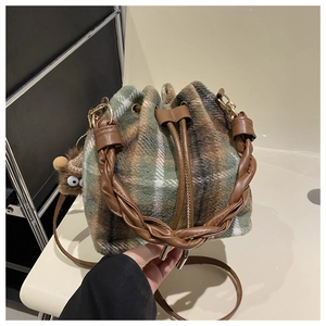 Close-up of green plaid bucket bag featuring a braided handle and plush eye charm