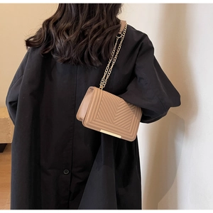 Detail view of a beige quilted crossbody bag with gold chain strap on a black coat