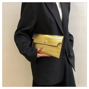 Detail of gold envelope clutch bag featuring premium crocodile embossed texture and metallic lock