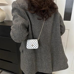 Mini white crossbody bag with black dots and golden chain strap shown in a home setting