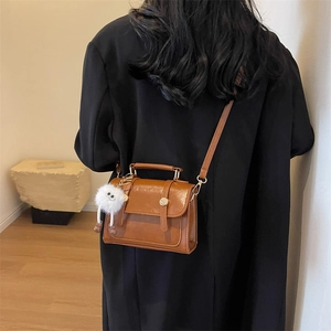 Brown vintage leather crossbody bag with flap and plush charm on a black coat