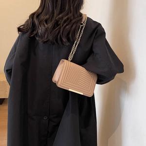 Chic quilted beige crossbody bag with gold chain strap and metal trim on black coat