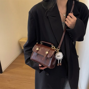Retro brown leather crossbody bag with metallic buckles and a cute plush charm accessory
